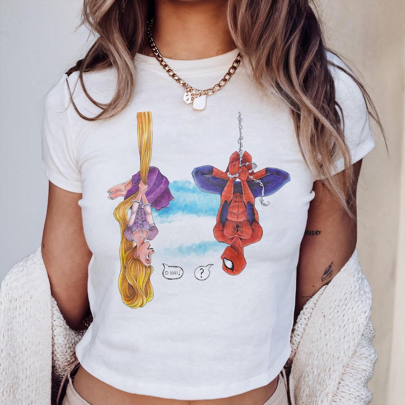 May include: White t-shirt featuring a cartoon illustration of Rapunzel and Spider-Man hanging upside down. Rapunzel is holding onto her long blonde hair, and Spider-Man is suspended by a web. The shirt has the text "O HAI?" in speech bubbles.