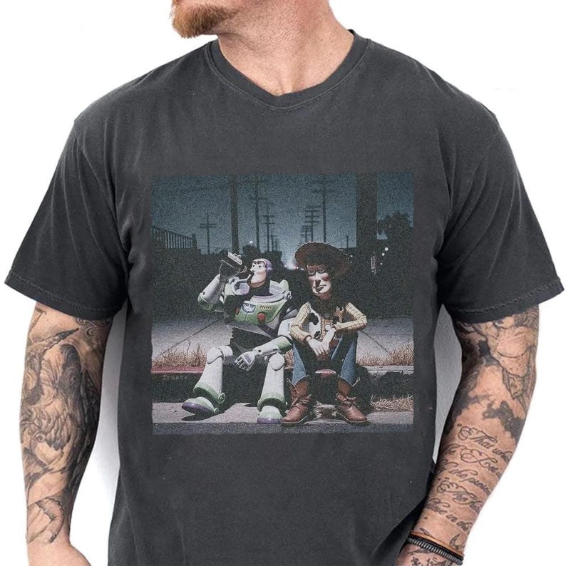 May include: Dark gray v-neck t-shirt featuring a graphic of Buzz Lightyear and Woody from Toy Story sitting together. Buzz is drinking from a bottle. The image has a vintage, slightly faded look.