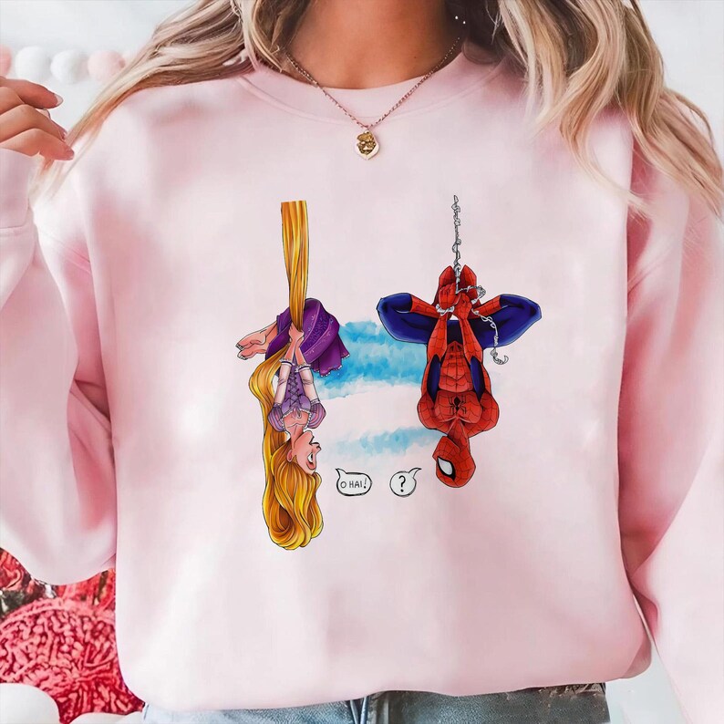May include: Pink sweatshirt featuring cartoon illustrations of Rapunzel and Spider-Man hanging upside down. Rapunzel is holding onto her long blonde hair, while Spider-Man hangs from a chain. The text "OHAI!" and a question mark are also included.
