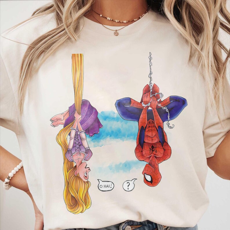 May include: Cream-colored t-shirt featuring cartoon illustrations of Rapunzel and Spider-Man hanging upside down. Rapunzel is holding her long blonde hair, and Spider-Man is hanging from a web. Speech bubbles say "O HAI!" and a question mark.