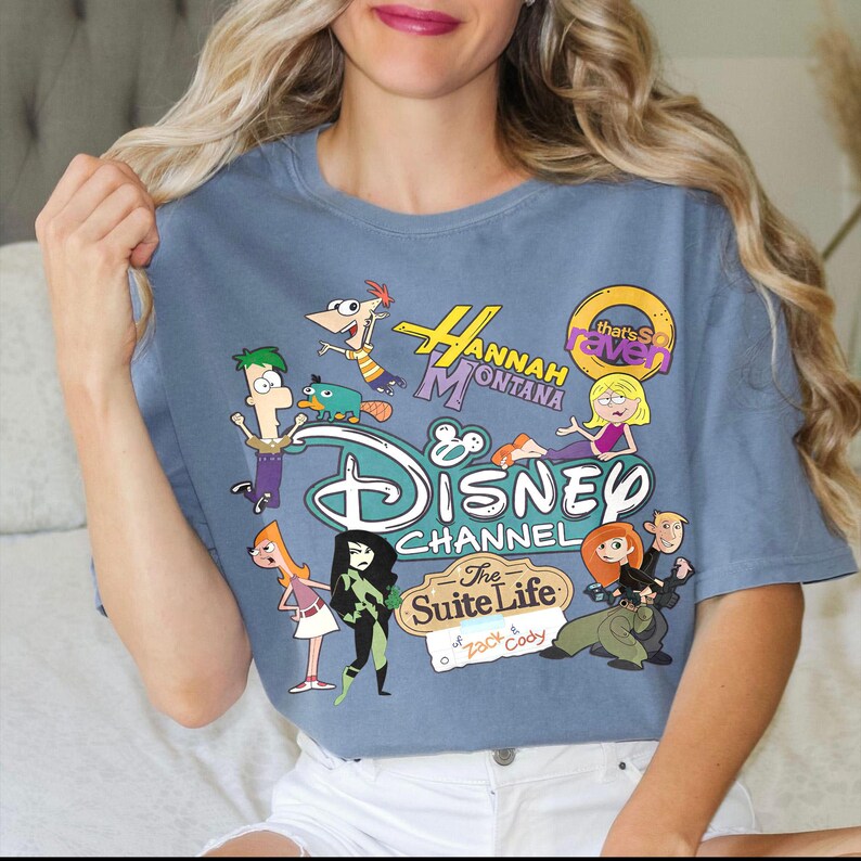 May include: Blue short-sleeved t-shirt with a Disney Channel graphic featuring characters from Hannah Montana, The Suite Life of Zack & Cody, and Kim Possible. The shirt has a crew neck and a relaxed fit.