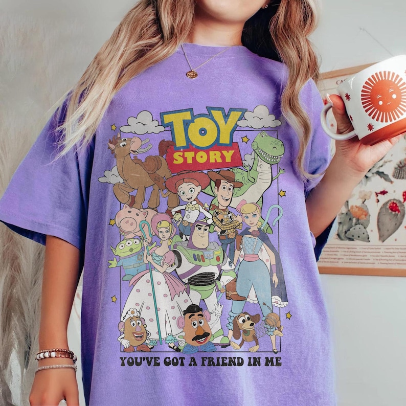 May include: A purple t-shirt featuring a graphic of characters from the animated film "Toy Story." The design includes the film's title and the phrase "You've Got a Friend in Me." The shirt has a relaxed fit.