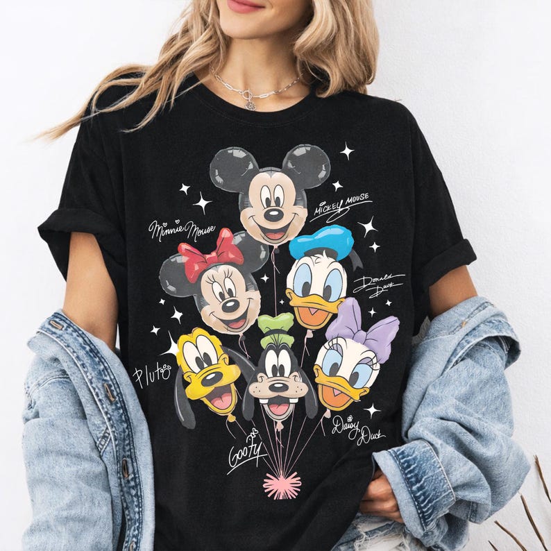 May include: A black short-sleeve t-shirt featuring a graphic print of Mickey Mouse, Minnie Mouse, Donald Duck, Pluto, Goofy, and Daisy Duck as balloons. The names of each character are written in white script next to their respective balloon faces.