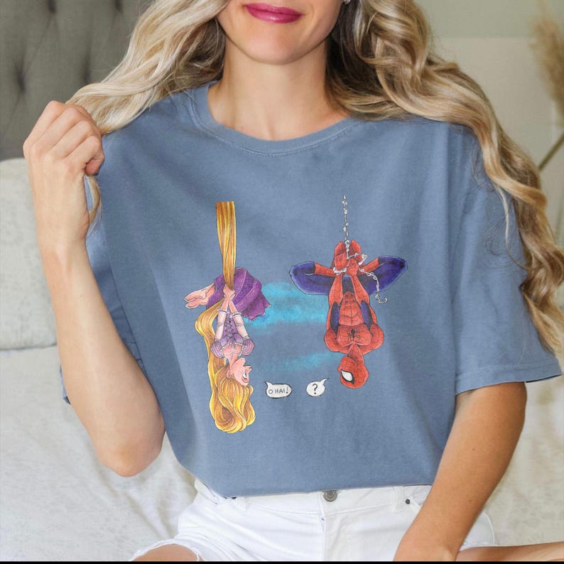 May include: A blue t-shirt featuring cartoon illustrations of Rapunzel and Spider-Man hanging upside down. Rapunzel is holding her long blonde hair, and Spider-Man is suspended by a web. Speech bubbles include the words "Oh Hai!" and a question mark.