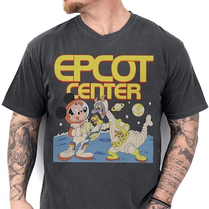 May include: Dark grey t-shirt with the text "EPCOT CENTER" in yellow and red. The graphic depicts Mickey Mouse and Figment in space suits on a planet with stars and planets. A vintage-style design.