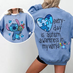Puede incluir: Sudadera azul claro con un personaje de dibujos animados sosteniendo una piruleta colorida y rodeado de corazones. La parte posterior tiene un diseño de rompecabezas en forma de corazón y el texto "every day is autism awareness in my world."