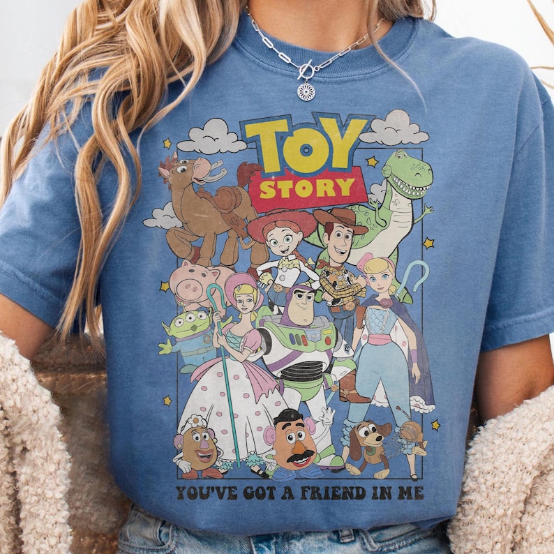 May include: A blue t-shirt featuring a graphic of characters from the animated film "Toy Story." The design includes the film's title and the phrase "You've Got a Friend in Me." The shirt showcases a variety of colorful cartoon characters.