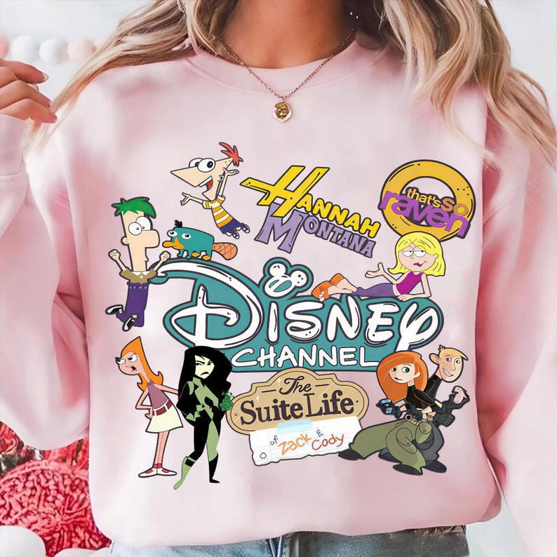 May include: Pale pink sweatshirt with a colourful Disney Channel design. The graphic includes characters and logos from shows such as "Hannah Montana", "That's So Raven", and "The Suite Life of Zack & Cody". A fun and nostalgic item.