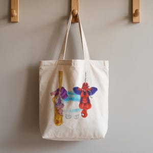 May include: A cream-colored tote bag featuring illustrations of Rapunzel and Spider-Man hanging upside down. Rapunzel is suspended by her hair, while Spider-Man hangs from a chain. The bag has a simple design with a light blue and white background.