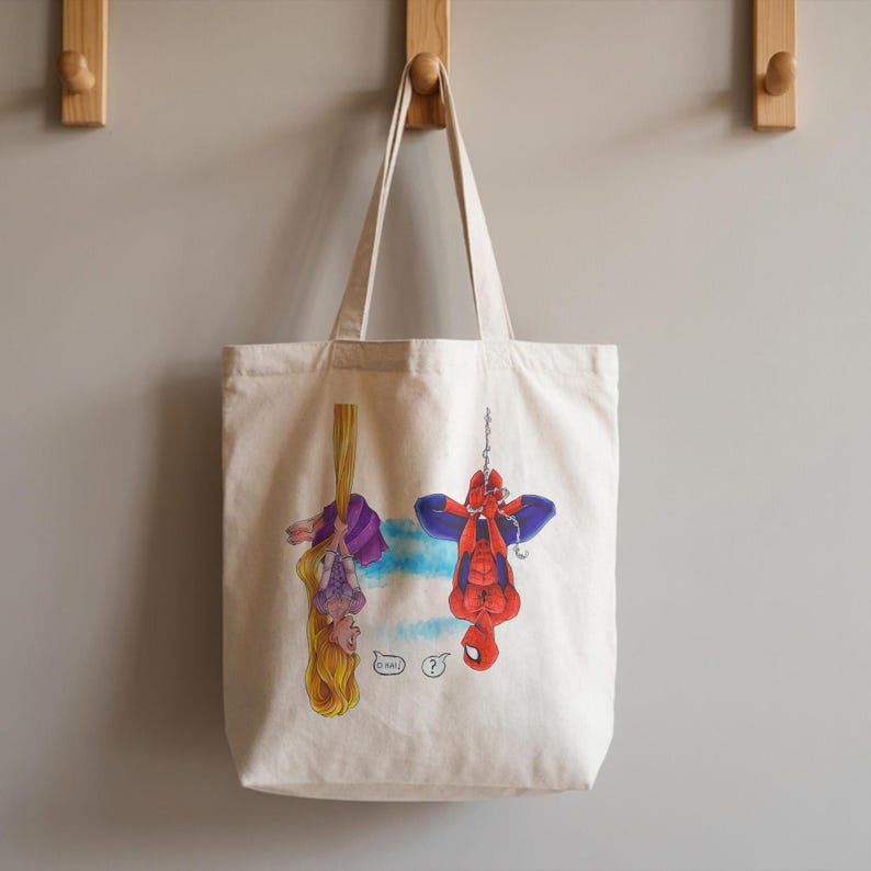 May include: A cream-colored tote bag featuring illustrations of Rapunzel and Spider-Man hanging upside down. Rapunzel is suspended by her hair, while Spider-Man hangs from a chain. The bag has a simple design with a light blue and white background.