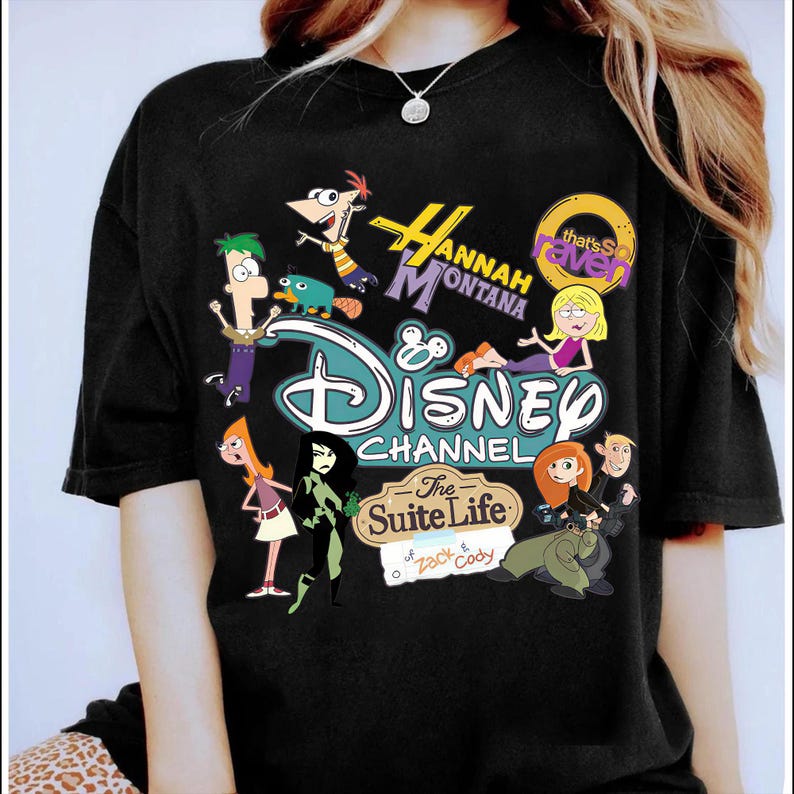 May include: Black t-shirt with a vibrant graphic showcasing Disney Channel characters such as Phineas and Ferb, Hannah Montana, Kim Possible, and The Suite Life of Zack & Cody. The Disney Channel logo is visible.
