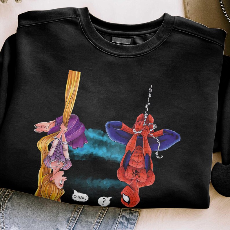 May include: Black sweatshirt featuring a cartoon illustration of Rapunzel and Spider-Man hanging upside down. Rapunzel is holding her long blonde hair, and Spider-Man is hanging from a web. Speech bubbles say "O HAI!" and "?".