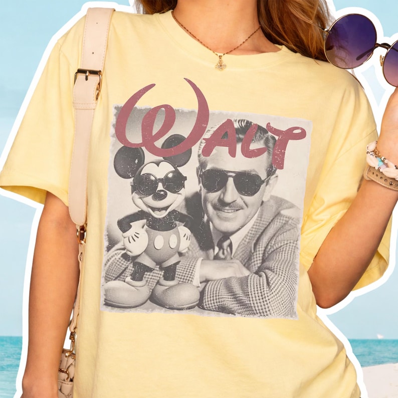 K&ouml;nnte beinhalten: Ein hellgelbes Kurzarm-T-Shirt mit einem schwarz-wei&szlig;en Grafikdruck von Walt Disney und Mickey Mouse, die beide eine Sonnenbrille tragen. Das Wort Walt ist in einer gro&szlig;en, verwaschenen kastanienbraunen Schreibschrift dar&uuml;ber gedruckt.