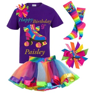 May include: Purple t-shirt featuring a rainbow roller skate graphic and the text "Happy Birthday 9th Paisley". A rainbow tulle skirt with colourful ribbon trim. A rainbow roller skate hair bow and a pair of rainbow striped knee-high socks.
