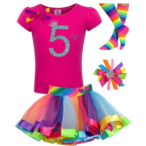 May include: A pink t-shirt with a glittery turquoise number 5 and a crown on top. The shirt is paired with a rainbow tulle skirt with colorful satin ribbon trim. A rainbow striped sock and a hair bow with a crown are also included.