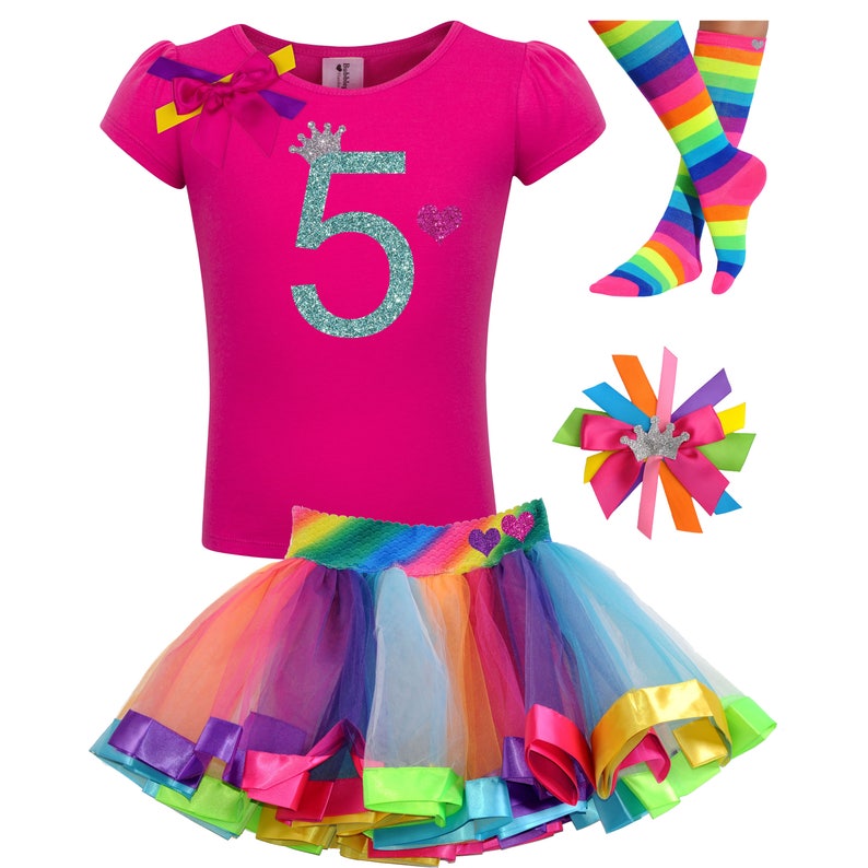 May include: A pink t-shirt with a glittery turquoise number 5 and a crown on top. The shirt is paired with a rainbow tulle skirt with colorful satin ribbon trim. A rainbow striped sock and a hair bow with a crown are also included.