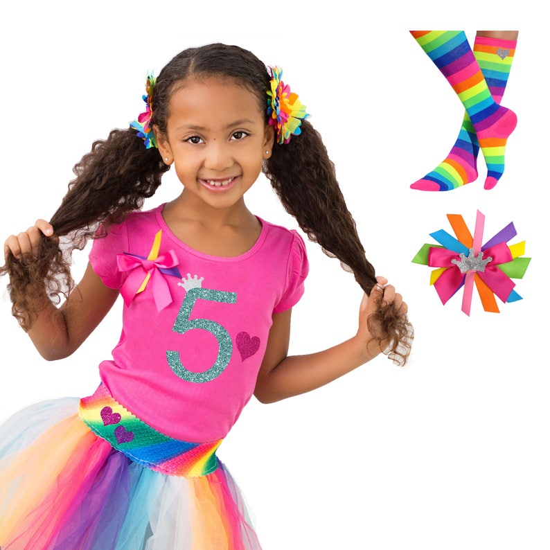 May include: A girl wearing a pink shirt with a glittery number 5 and a crown on it. She is also wearing a rainbow tutu and has rainbow hair bows. The image also includes a pair of rainbow socks and a rainbow hair bow with a crown.