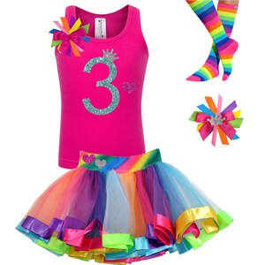 May include: A pink tank top with a glittery teal number "3" and a crown on it. The tank top is paired with a rainbow tulle skirt with colorful satin ribbon trim. A rainbow striped knee-high sock and a rainbow hair bow with a crown are also included.