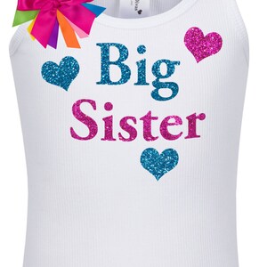 May include: White tank top with the words "Big Sister" in blue and pink glitter lettering. There are three glitter hearts, two blue and one pink, on the shirt.