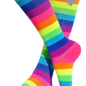 May include: A pair of knee-high socks with a rainbow stripe pattern. The socks are pink, orange, yellow, green, blue, purple, and pink. One sock has a silver glitter heart on the top.