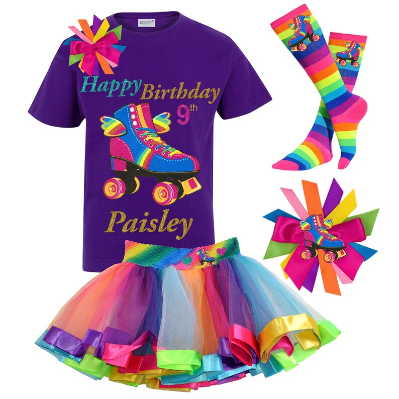 May include: Purple t-shirt featuring a rainbow roller skate graphic and the text "Happy Birthday 9th Paisley". A rainbow tulle skirt with colourful ribbon trim. A rainbow roller skate hair bow and a pair of rainbow striped knee-high socks.