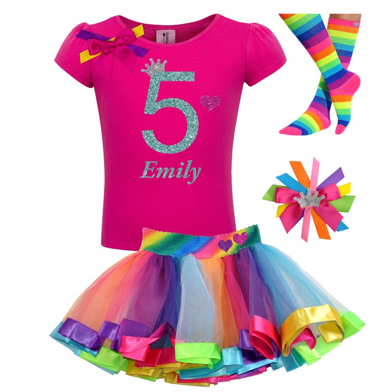May include: A pink t-shirt with a glittery turquoise number 5 and a crown, the name "Emily" is written below the number. A rainbow tulle skirt with a rainbow stripe waistband and a matching rainbow striped bow with a crown. A pair of rainbow striped socks.