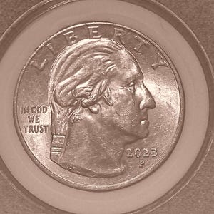 Pode incluir: Uma moeda de um quarto de dólar americano de cor prateada com o perfil de George Washington virado para a direita. O texto LIBERTY está arqueado no topo, IN GOD WE TRUST à esquerda e o ano 2023 com a marca da casa da moeda P à direita.
