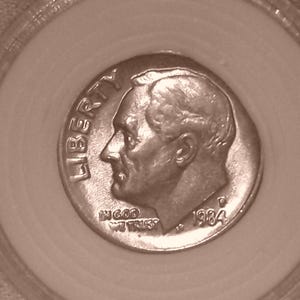 May include: A 1984 United States dime coin featuring the profile of Franklin D. Roosevelt facing left. The word LIBERTY is arched along the left edge, with IN GOD WE TRUST below the chin and the year 1984 and a P mint mark on the right side.