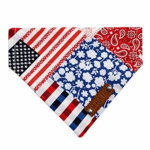 May include: A triangular pet bandana featuring a patchwork design of the American flag, a red paisley pattern, and a blue floral print. A brown leather tag with the name MILLIE embossed in capital letters is attached with two silver metal rivets.
