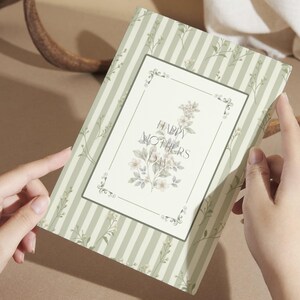 Peut inclure: Une carte de vœux avec un motif floral et le texte "HAPPY MOTHERS DAY". La carte a un fond rayé dans les tons de vert et de blanc. La carte est tenue par deux mains.