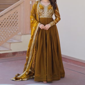 May include: A mustard-coloured formal dress with detailed gold embroidery on the bodice and sleeves. The dress has a flowing skirt and is accompanied by a matching shawl with gold detailing. Suitable for special occasions.