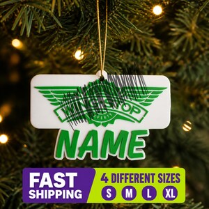 May include: A white, rectangular hanging ornament featuring a green Wingstop logo with wings and the word NAME in large green letters below it. The ornament is suspended by a thin gold string and includes a graphic indicating four different sizes.