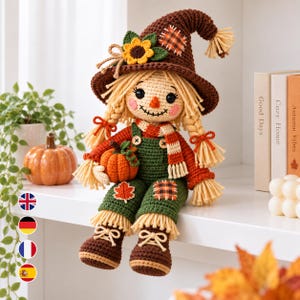 May include: A crocheted scarecrow doll wearing a brown hat with a sunflower, a red long-sleeved shirt, and green overalls with patches. The doll has blonde yarn hair in braids, a stitched face, and holds a small orange crocheted pumpkin.
