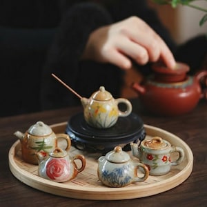 May include: A set of three ceramic mugs with a speckled, matte finish. The mugs are in cream, light grey, and dark grey. Each mug has a simple, minimalist design, ideal for coffee or tea.