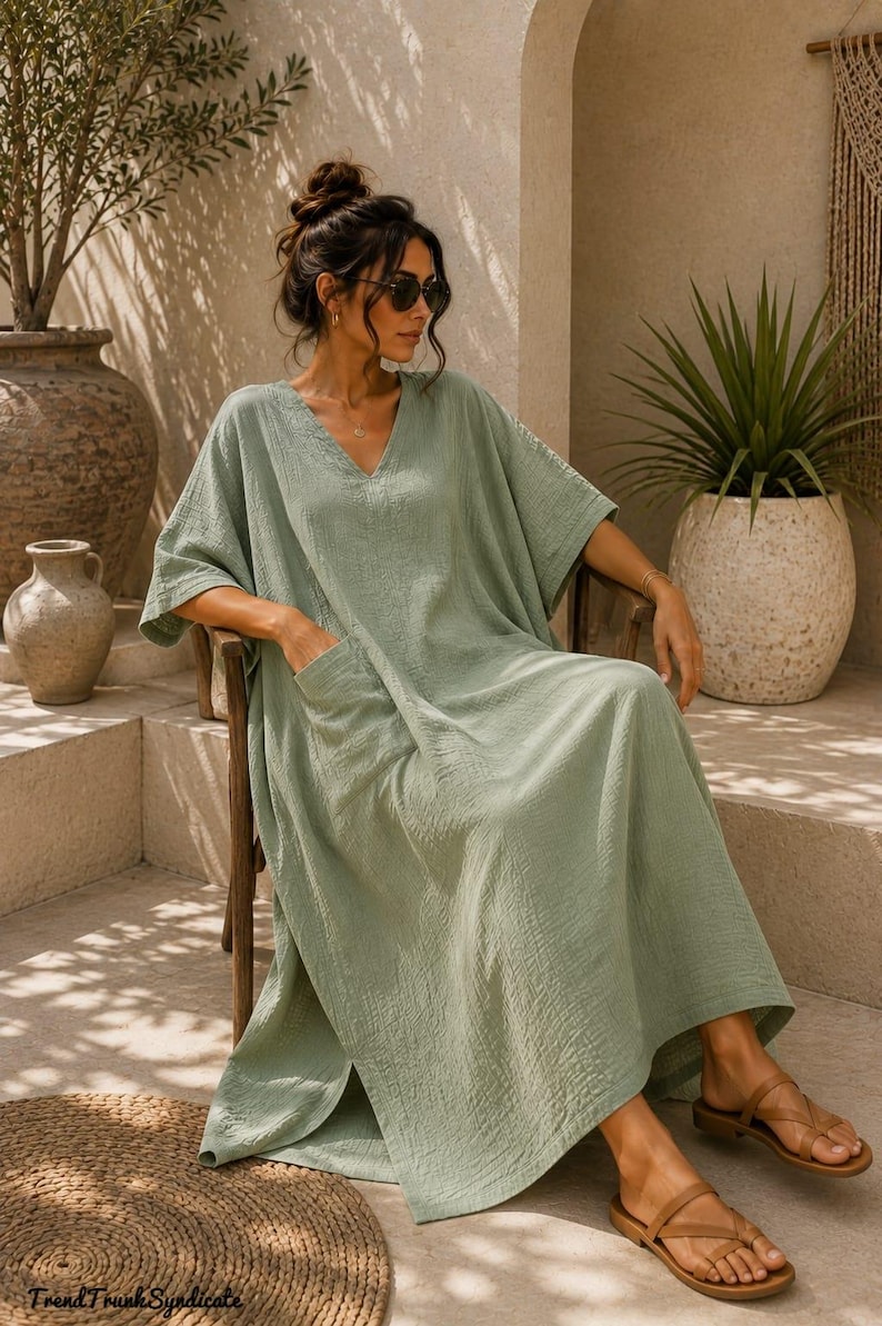 May include: A sage green midi-length kaftan dress with a V-neckline, short wide sleeves, and side pockets. The fabric has a textured, crinkled appearance. The text "TrendTrunkSyndicate" is visible in the bottom left corner of the image.