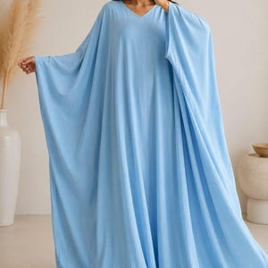 Op de afbeelding: Een vloerlange, lichtblauwe kaftan-jurk met een V-hals en wijde, vloeiende mouwen. Het kledingstuk is gemaakt van een effen, lichtgewicht stof die losjes vanaf de schouders tot aan de vloer valt, wat zorgt voor een volumineus silhouet.