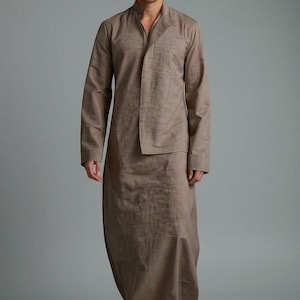 Peut inclure: Ensemble deux pièces marron clair, composé d'un haut à manches longues et d'une jupe assortie. Le haut a un col mandarin et un devant drapé. La jupe est longue. L'ensemble est associé à des baskets blanches. Le texte "TRENDTRUNKSYNDICATE" est en bas.