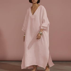 May include: A pale pink linen dress with a V-neck and wide sleeves. The floor-length dress has side slits and is worn with sandals. The image includes the text "Trend Trunk Syndicate".