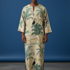 May include: A beige, long-sleeved caftan with a V-neck and a tropical print featuring toucans, leopards, palm trees, and other wildlife. The caftan is floor-length and has side slits. The text "Trend Trunk Syndicate" is at the bottom.
