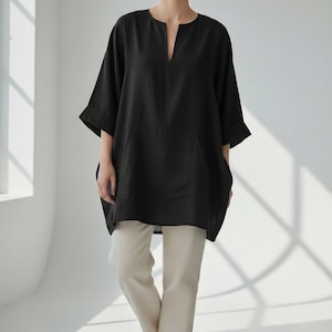 Könnte beinhalten: Ein schwarzes Tunika-Oberteil mit V-Ausschnitt und kurzen Ärmeln wird mit cremefarbenen Hosen und weißen Turnschuhen kombiniert. Das Outfit ist schlicht und modern. Der Text "Trend Trunk Syndicate" befindet sich unten links.
