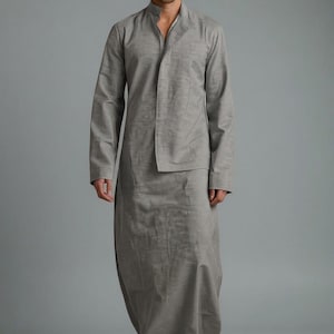 May include: A light gray, long-sleeved tunic and matching skirt. The tunic has a mandarin collar and a front panel. The skirt is floor-length. The outfit is made of a lightweight fabric. The model is wearing white sneakers.