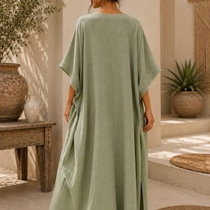 May include: A sage green maxi kaftan dress with a textured, crinkled fabric finish, wide short sleeves, and side slits. The garment features a loose, flowing silhouette and a simple round neckline. The text TrendTrunkSyndicate is visible.
