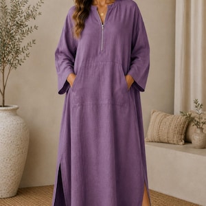 May include: A long-sleeved, floor-length purple dress featuring a front zipper closure at the neckline, a large front kangaroo pocket, and high side slits along the hem. The garment has a loose, relaxed fit with wide sleeves and a simple collar.