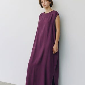 May include: A sleeveless, floor-length plum-colored dress with a round neckline and side slits. The dress is worn with white sneakers. The text "Trend Trunk Syndicate" is visible at the bottom left.