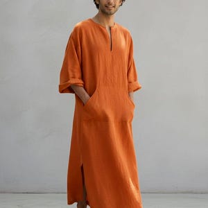 May include: An orange linen caftan with a split hem and a front pocket. The caftan has a relaxed fit and short sleeves. The model is wearing the caftan. The text "TRENDTRUNKSYNDICATE" is at the bottom of the image.