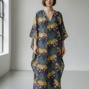 May include: A long, flowing, V-neck dress with a navy blue background and a repeating pattern of yellow leopards and green foliage. The dress has wide sleeves and a relaxed fit, suitable for casual wear.