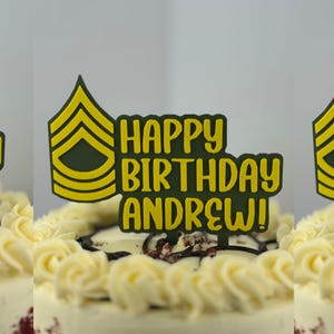 Puede incluir: Una tarta decorada con glaseado blanco y un adorno para tarta que dice "HAPPY BIRTHDAY ANDREW!" en letras amarillas. El adorno para tarta también presenta una insignia militar amarilla y verde.