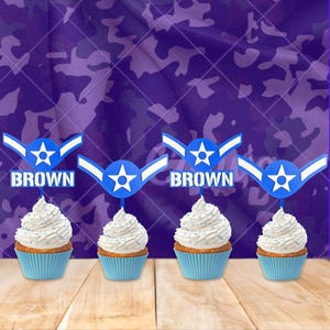 May include: Four cupcakes in blue liners with white frosting and blue sprinkles. Each cupcake has a blue and white topper with a star and the word "BROWN". The background is a purple camouflage pattern.