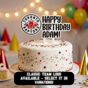 Puede incluir: Un pastel redondo blanco decorado con chispas rojas y negras en forma de estrella. Dos adornos para pastel están insertados en la parte superior: un logotipo circular del equipo Toronto Raptors y un letrero blanco con el texto negro Happy Birthday Adam!