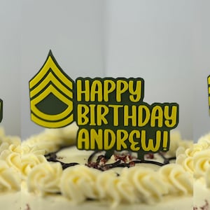 Könnte beinhalten: Ein Geburtstagskuchen mit weißem Zuckerguss und roter Füllung. Er ist mit einem grünen und gelben Tortenaufsatz mit der Aufschrift "Happy Birthday Andrew!" und einem militärischen Dienstgradabzeichen verziert.